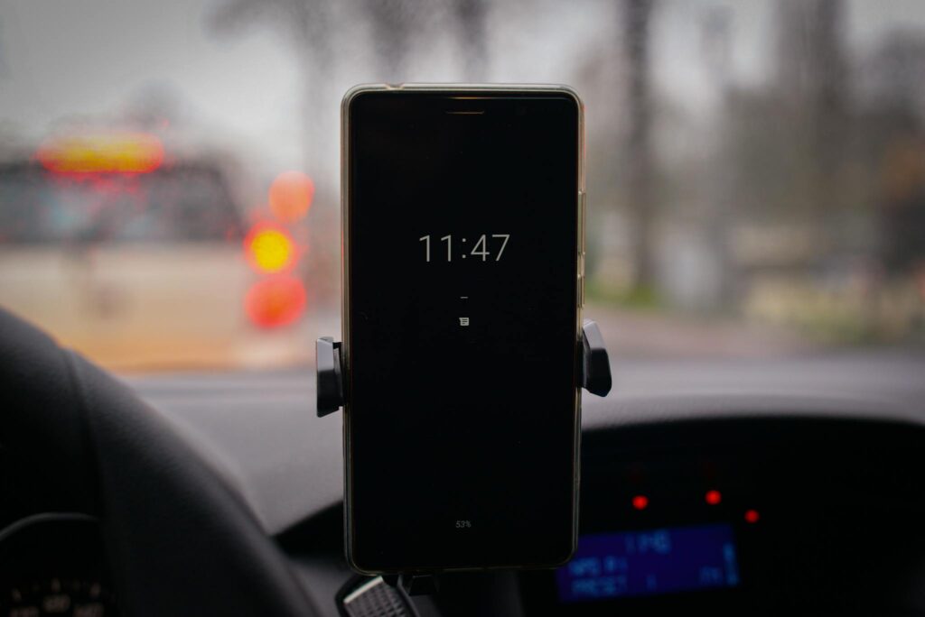 A smartphone mounted in a car with its screen showing the time in a blurred traffic environment.