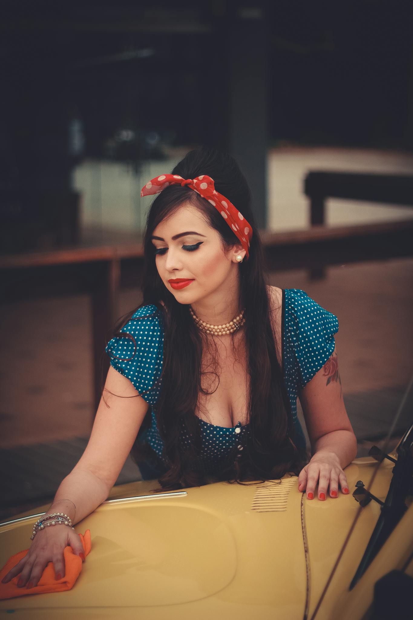 A woman in vintage attire wipes a classic yellow car. Retro aesthetics enhance the nostalgic ambiance.
