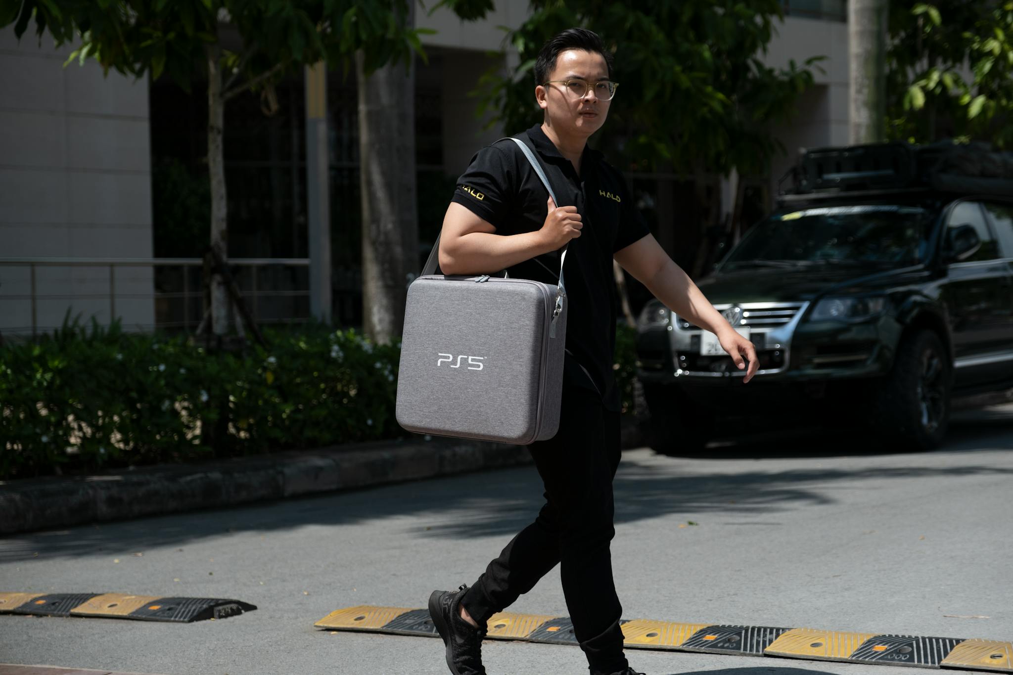 Asian man walking outdoors with a PS5 bag, showcasing urban lifestyle and fashion.