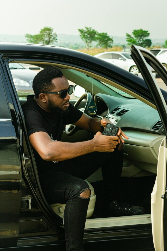 Casual portrait of a young man with sunglasses using a smartphone in a parked car.