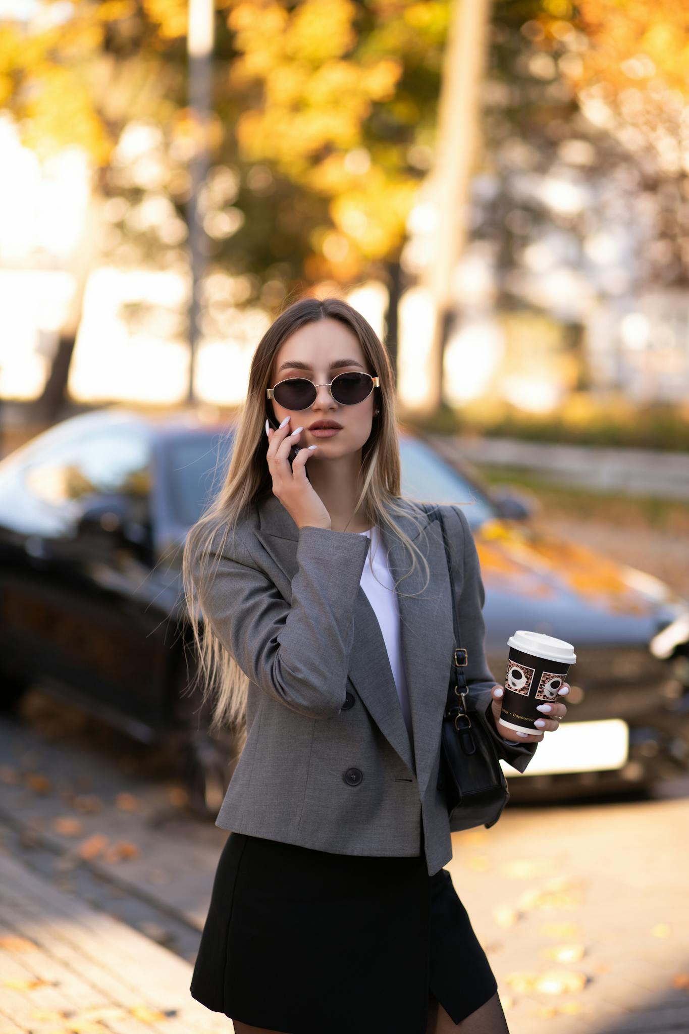Fashionable woman in autumn outfit with coffee and phone outdoors.