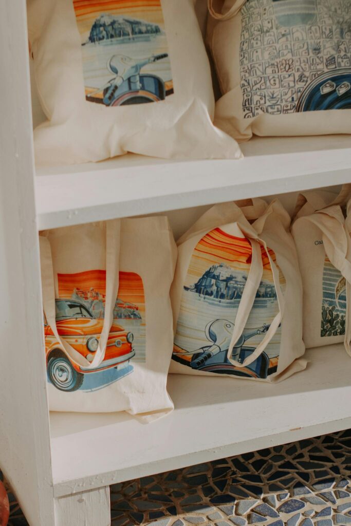 Vibrantly designed canvas tote bags neatly displayed on a wooden shelf, showcasing artistic prints.