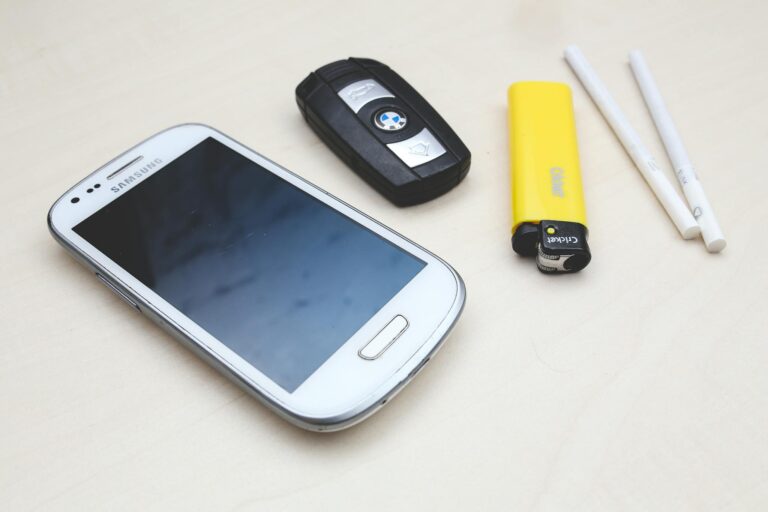 Flat lay of everyday items: smartphone, car key, lighter, and cigarettes on a table.