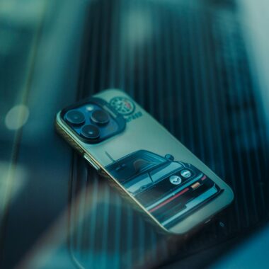 Smartphone featuring a vintage car-themed case placed on a reflective glass surface, showcasing stylish design.