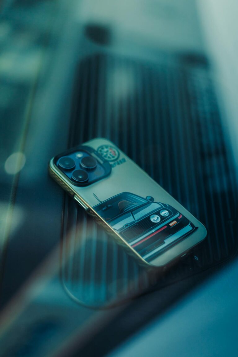 Smartphone featuring a vintage car-themed case placed on a reflective glass surface, showcasing stylish design.