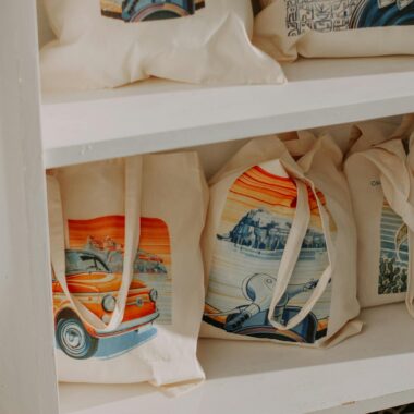 Vibrantly designed canvas tote bags neatly displayed on a wooden shelf, showcasing artistic prints.